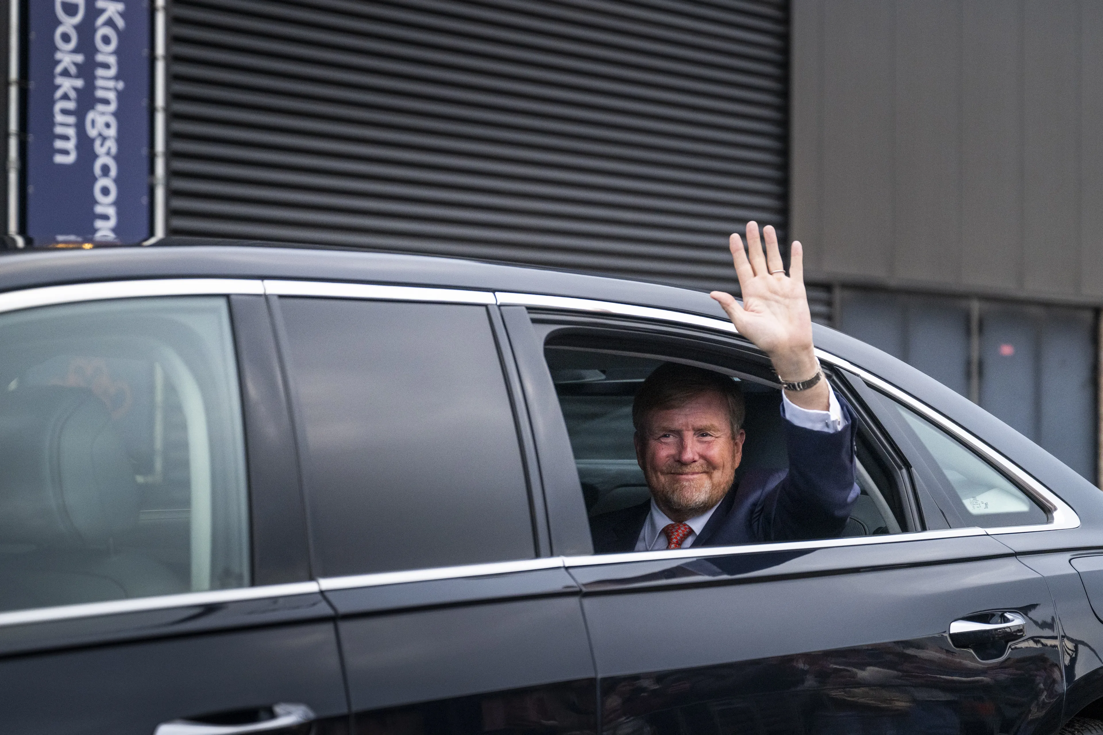 De koning zwaait na afloop van een bezoek vanuit zijn auto.