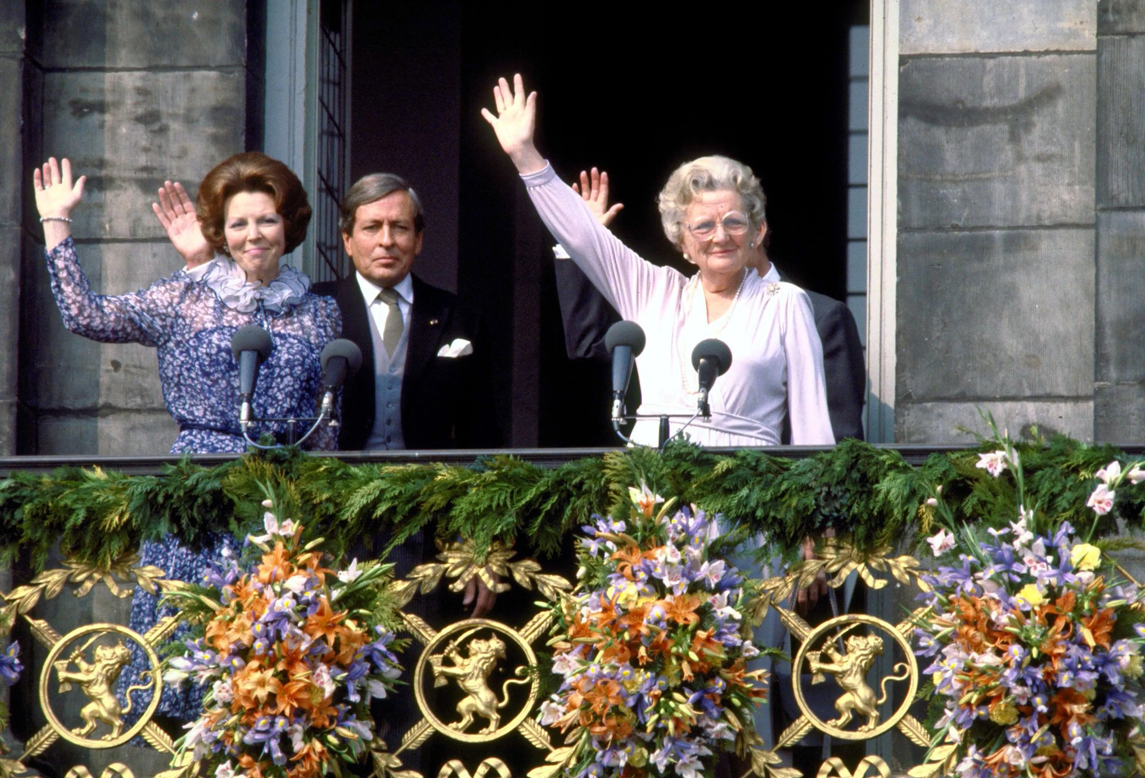 Beatrix zwaait vanaf het paleisbalkon naar de menigte, maar ziet ook de protesten.