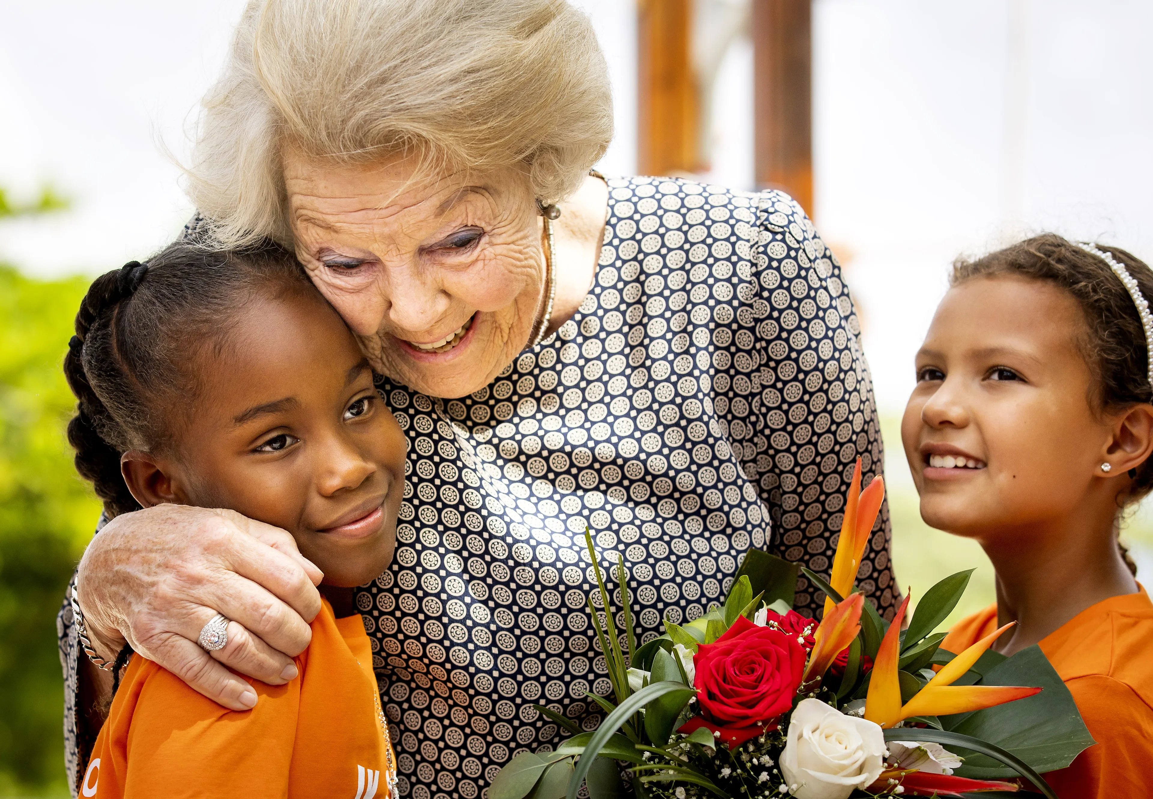 Prinses Beatrix knuffelt een meisje in een Jantje Beton-speeltuin op Aruba (2023).