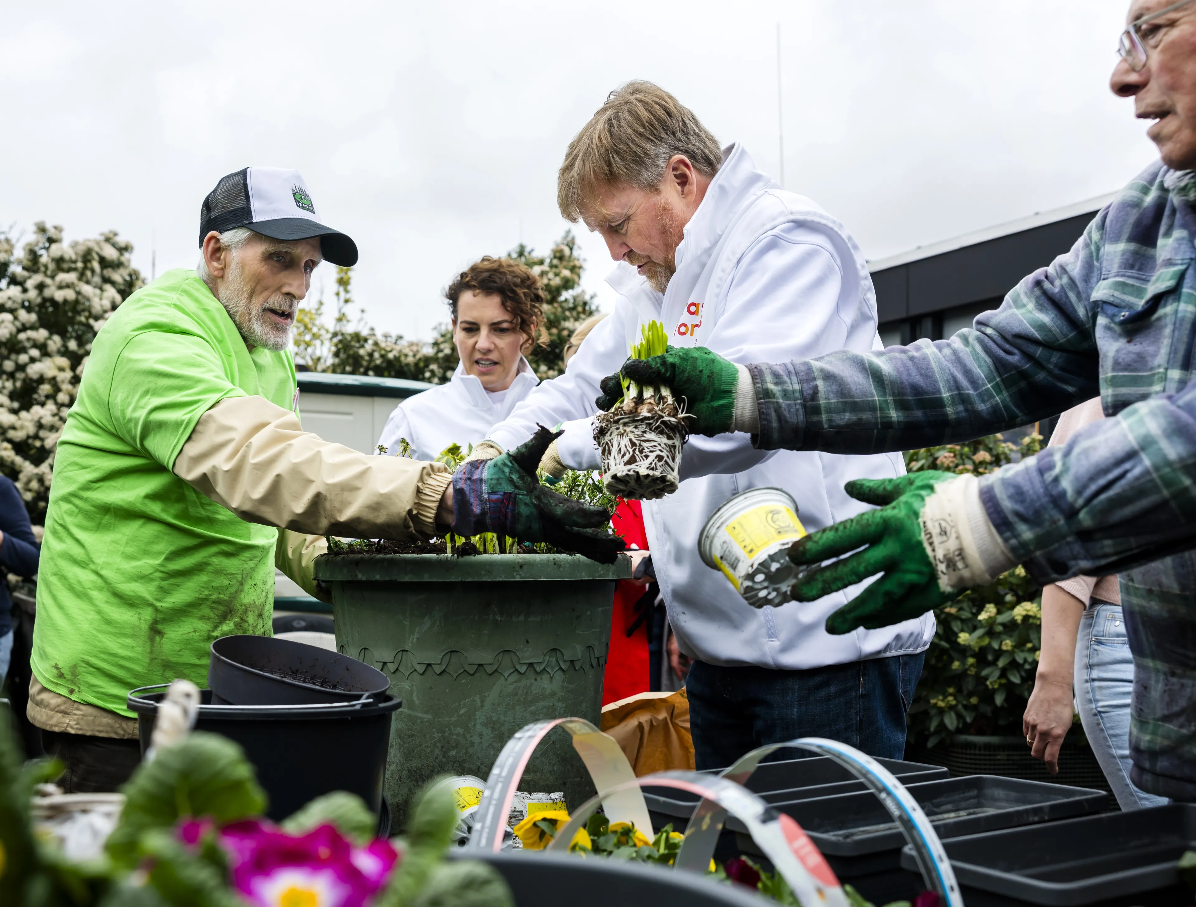 Koning Willem-Alexander trotseert de regen en plant met bewoners bloemetjes om de tuin mee op te vrolijken.