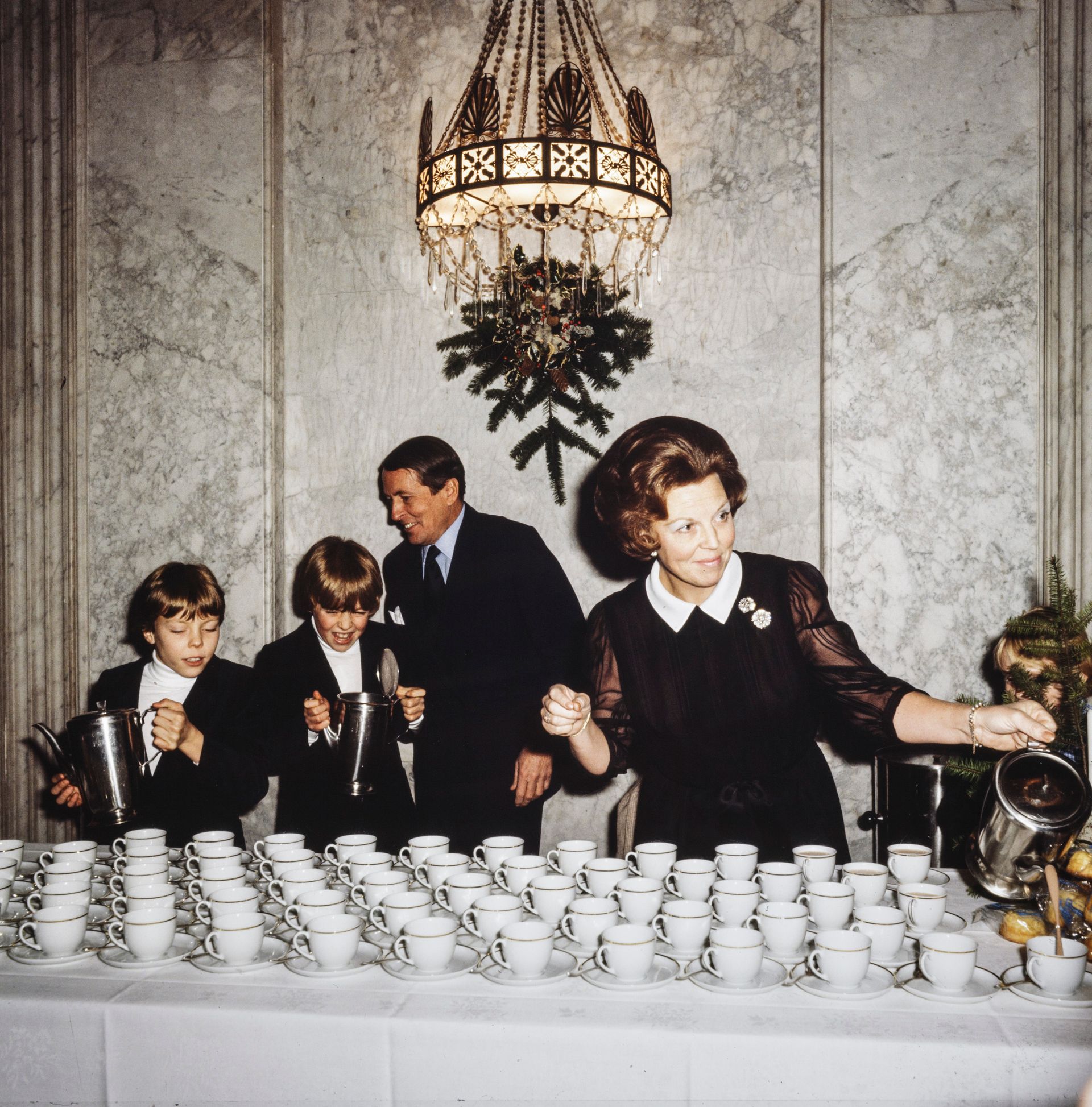 Koningin Beatrix, prins Claus, prins Constantijn en prins Johan Friso delen chocolademelk en broodjes uit aan het personeel.