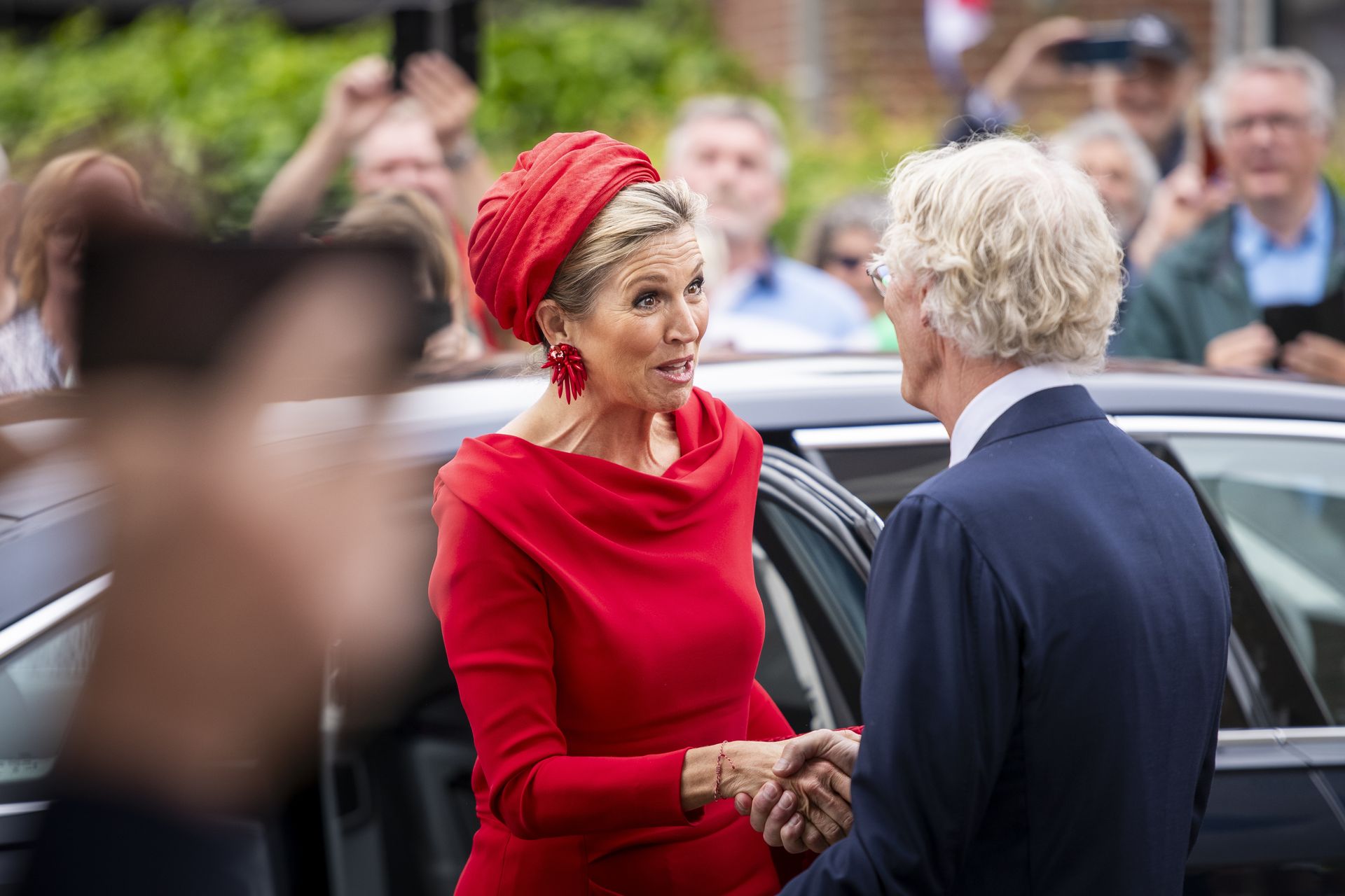 Koningin Máxima komt aan in een klassieke Hinderlooper-rode jurk.