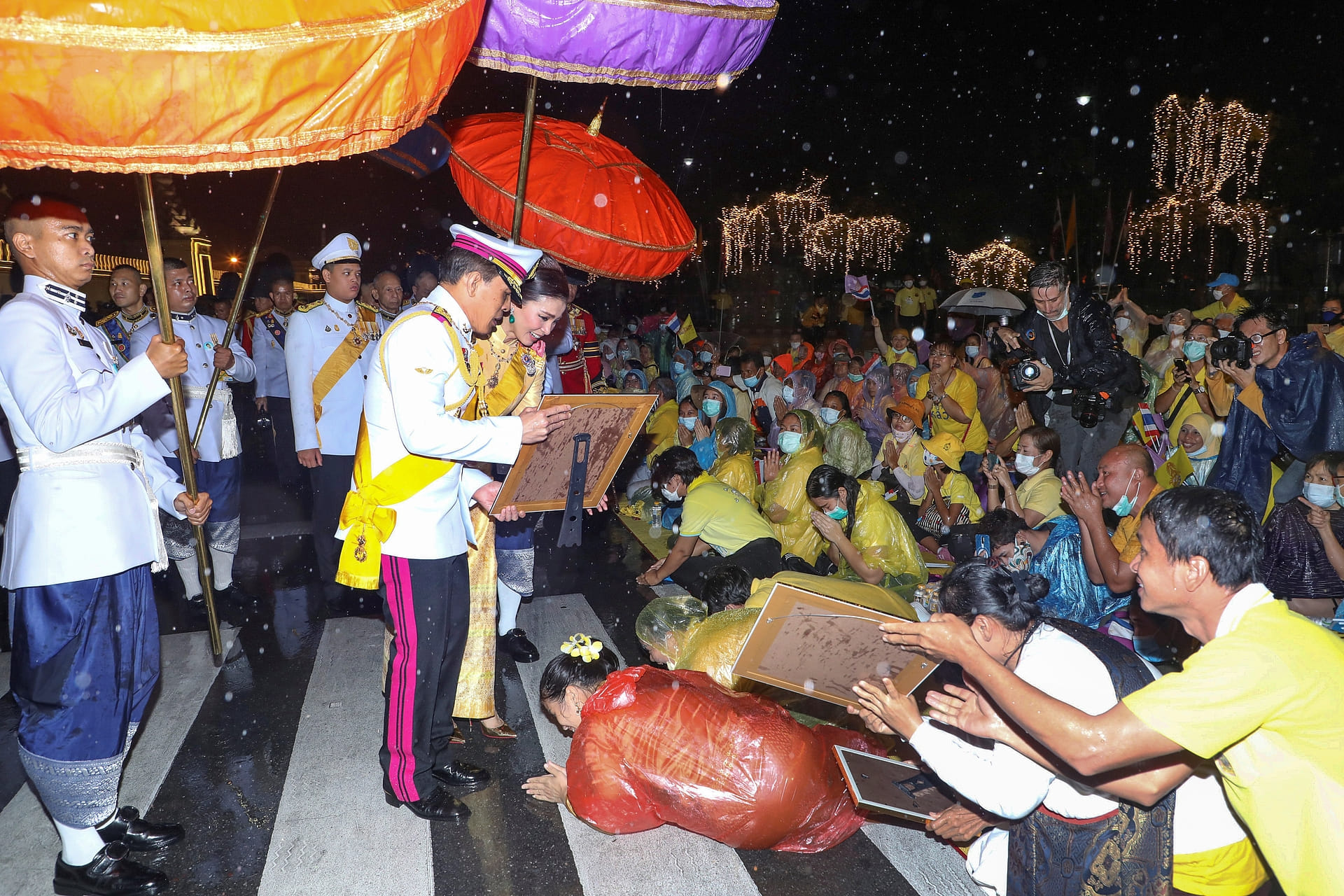Vajiralongkorn en Suthida met prins Dipangkorn Rasmijoti begroeten tegenbetogers buiten het Grand