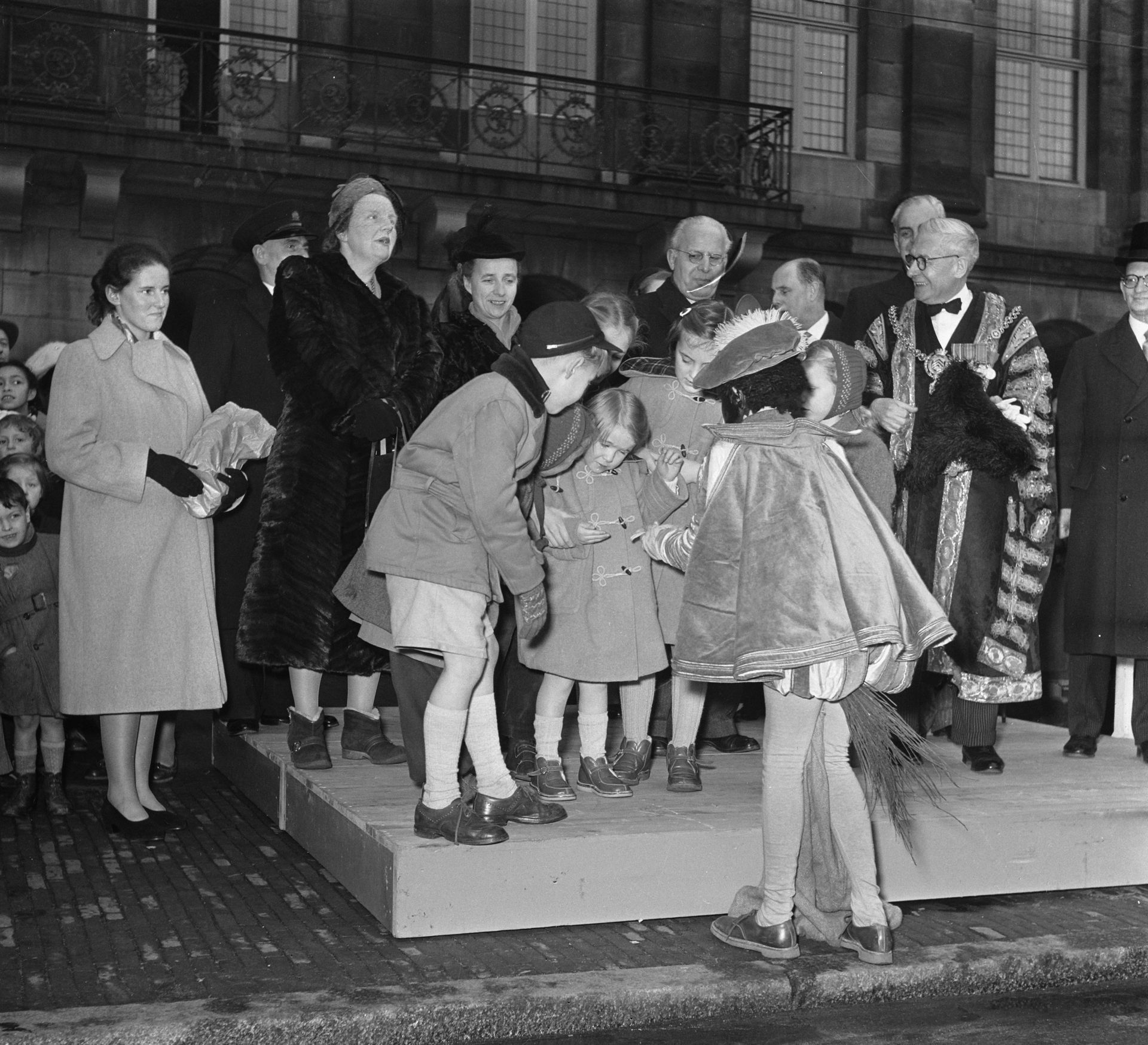 De prinsessen Christina en Margriet krijgen pepernoten uit de hand van een klein Pietje. - Paleis op de Dam 1952.
