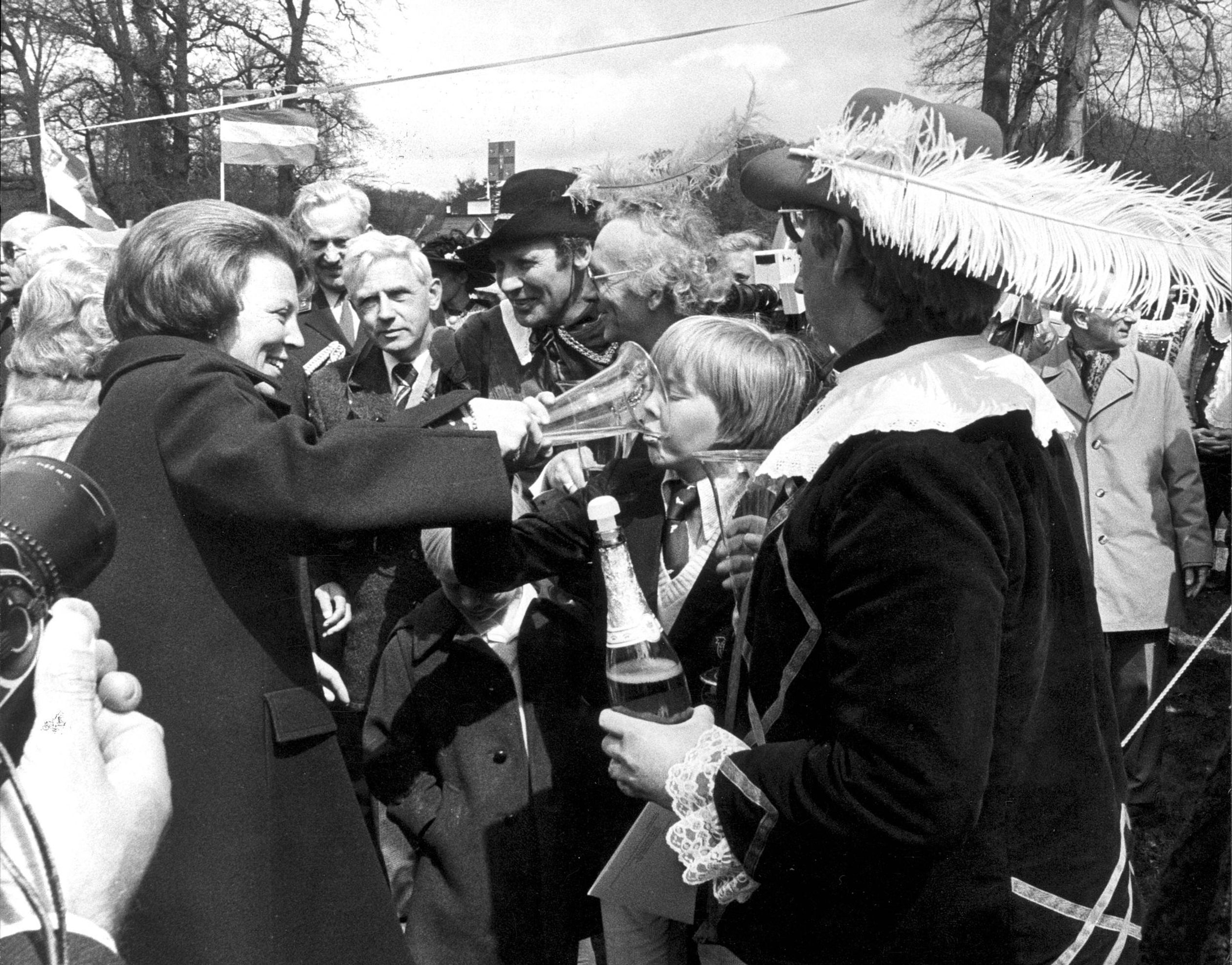 Wat een bijzondere kiekje! Prinses Beatrix geeft haar zoon Prins Alexander een slokje champagne uit een speciaal glas dat haar wordt aangeboden tijdens een wandeling voor het paleis (1979).
