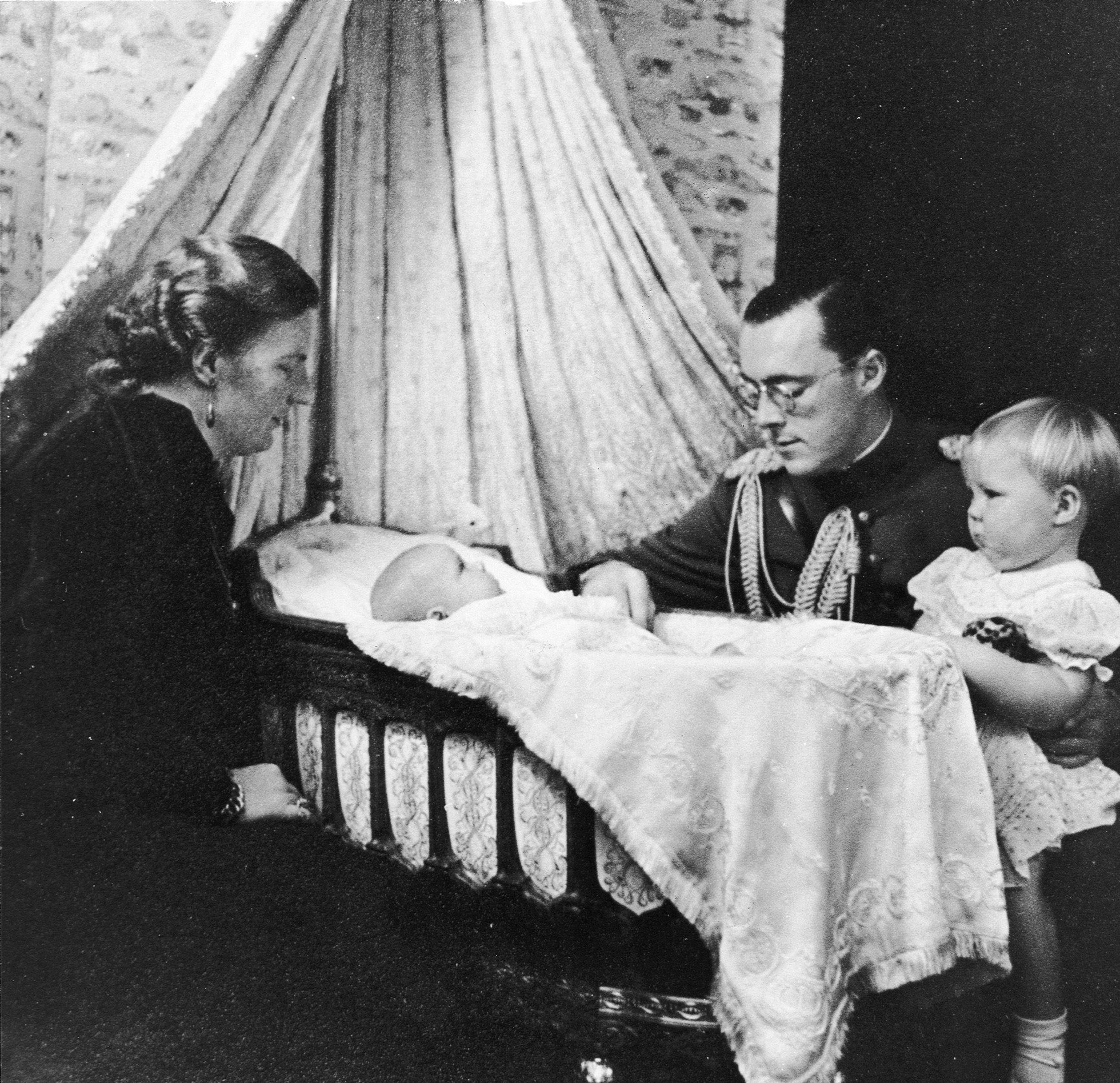 Prinses Irene in de wieg, omring door haar ouders en zusje prinses Beatrix.