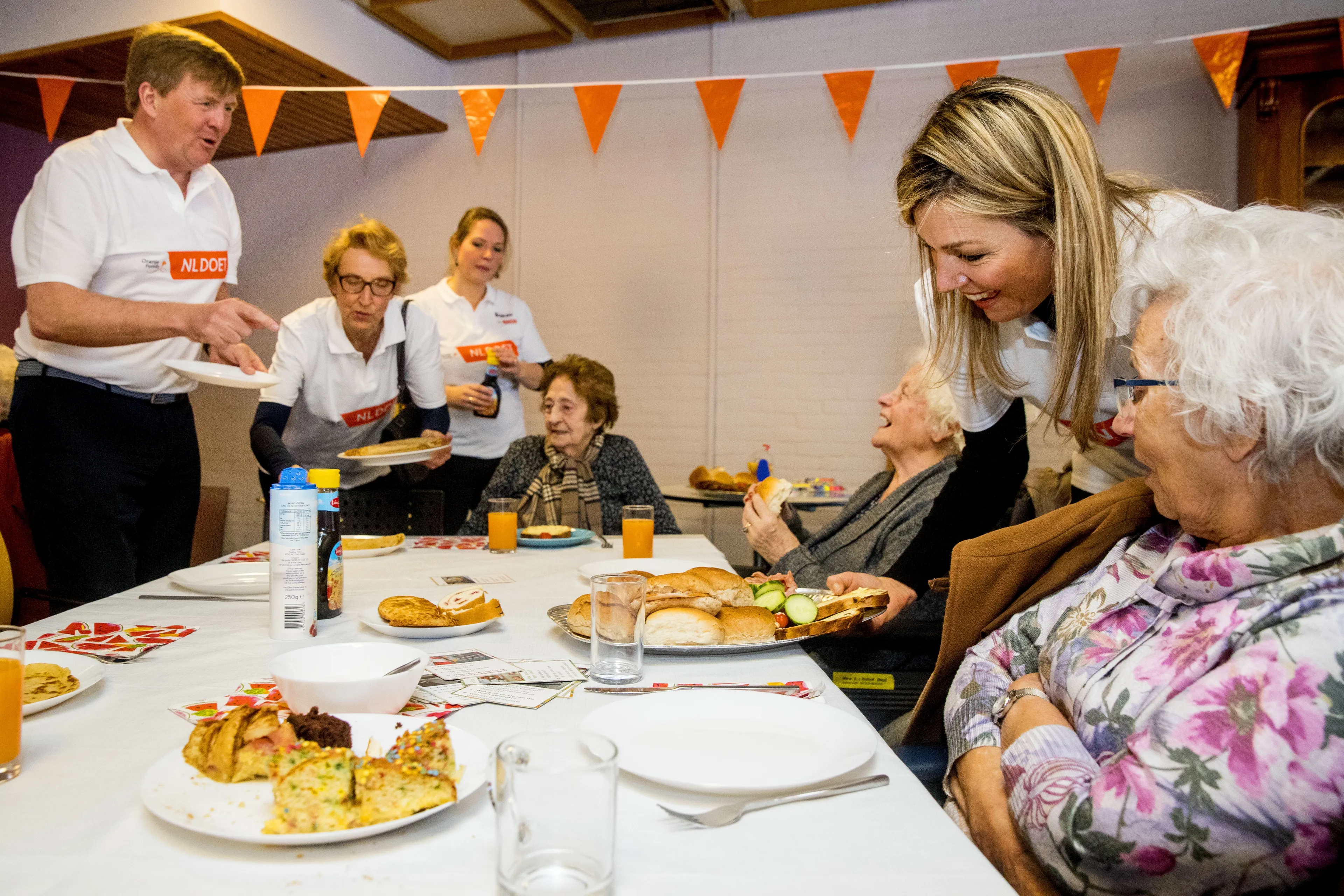 De koning en koningin delen de broodjes uit.